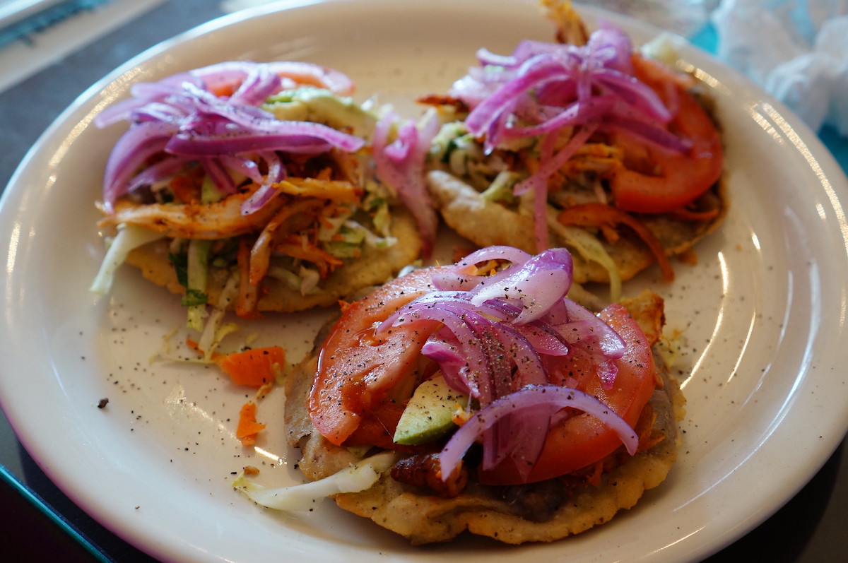 cierre un plato con tres panuchos, tortillas fritas planas cubiertas con tomate, repollo, aguacate y cebolla roja