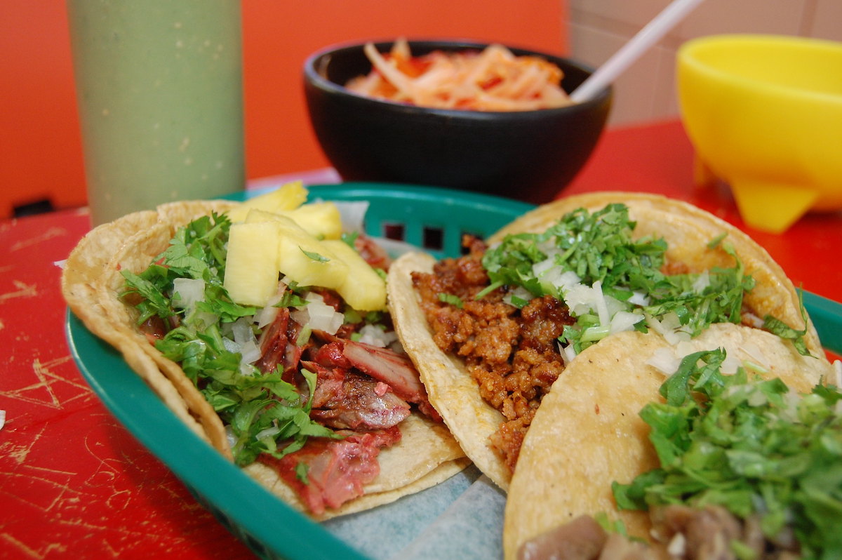 Cerca de tres tacos en una canasta de plástico verde sobre una mesa pintada de rojo