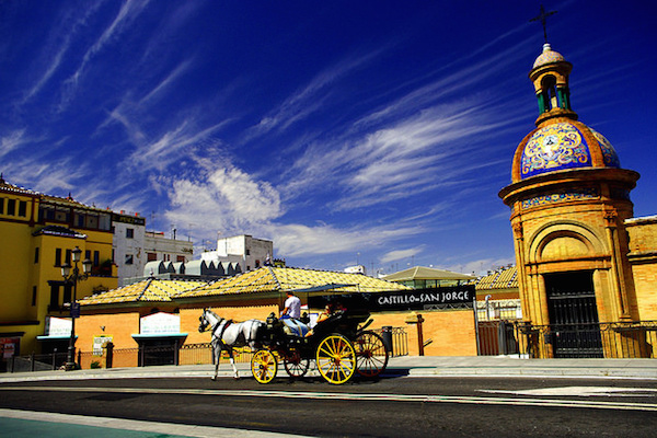 Un caballo y un carruaje pasan por el Mercado de Triana y se adentran en el barrio de Triana. Echa un vistazo a nuestra Guía de viajes definitiva a Sevilla para saber qué hacer en Triana, Sevilla. 