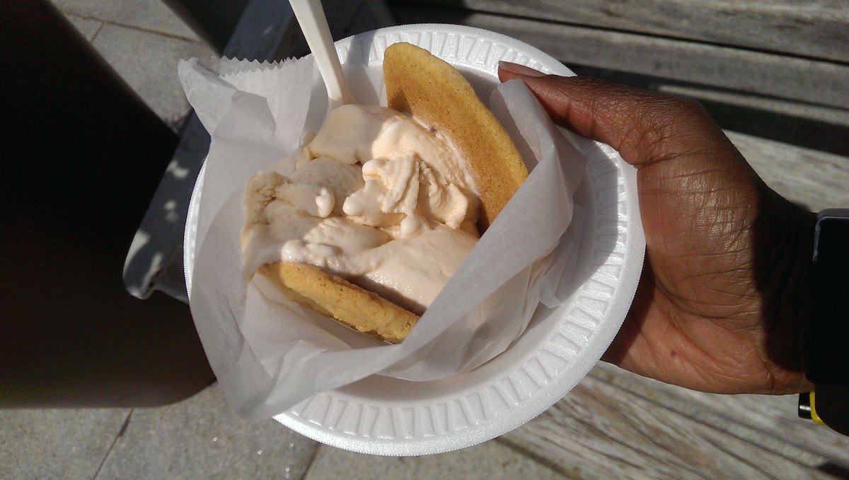 Una persona sostiene un tazón blanco con un sándwich de helado sobre papel