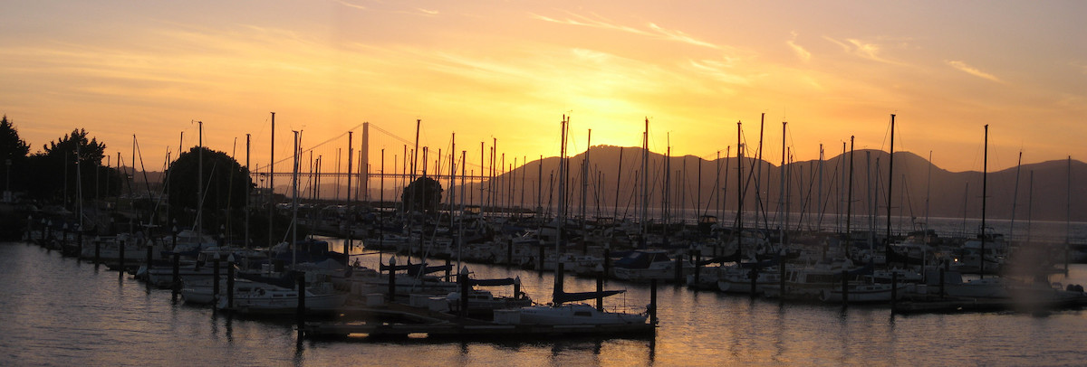Los veleros atracados se alinean en el agua de la Bahía de San Francisco con la puesta de sol detrás del puente Golden Gate en el fondo