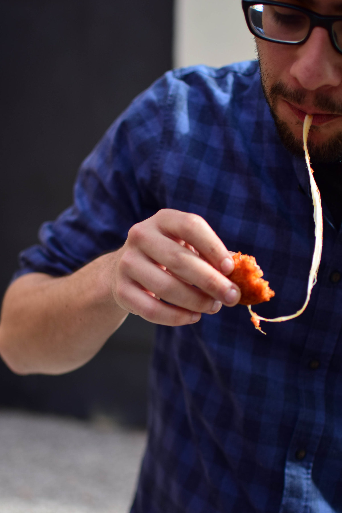 primer plano de un hombre comiendo un suministro, una bola de pan y queso y un amigo, con una larga cadena de queso que se extiende desde su boca