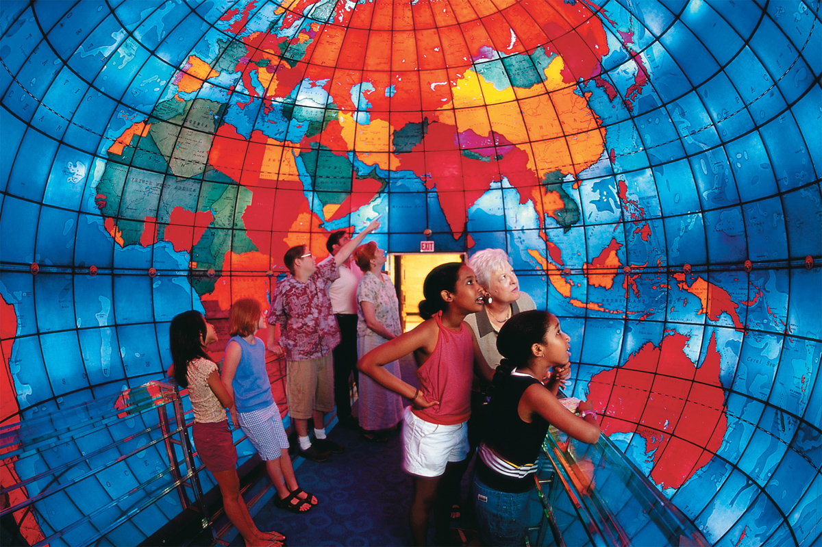 Un grupo de personas de diferentes edades en una habitación en forma de cúpula con las paredes decoradas con un colorido mapamundi. El Mapparium es una verdadera joya escondida de Boston.