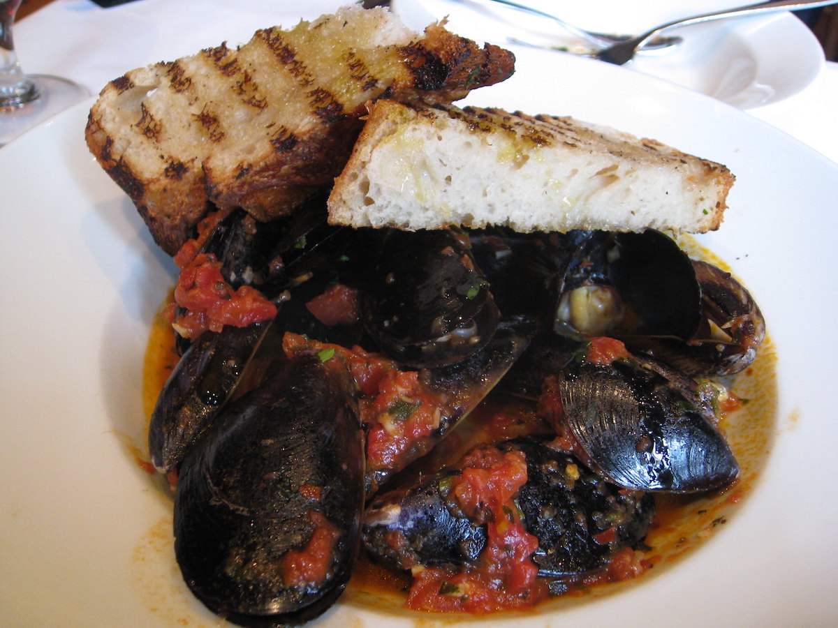 Primer plano de un plato de mejillones guisados ​​con salsa de tomate y pan caliente encima