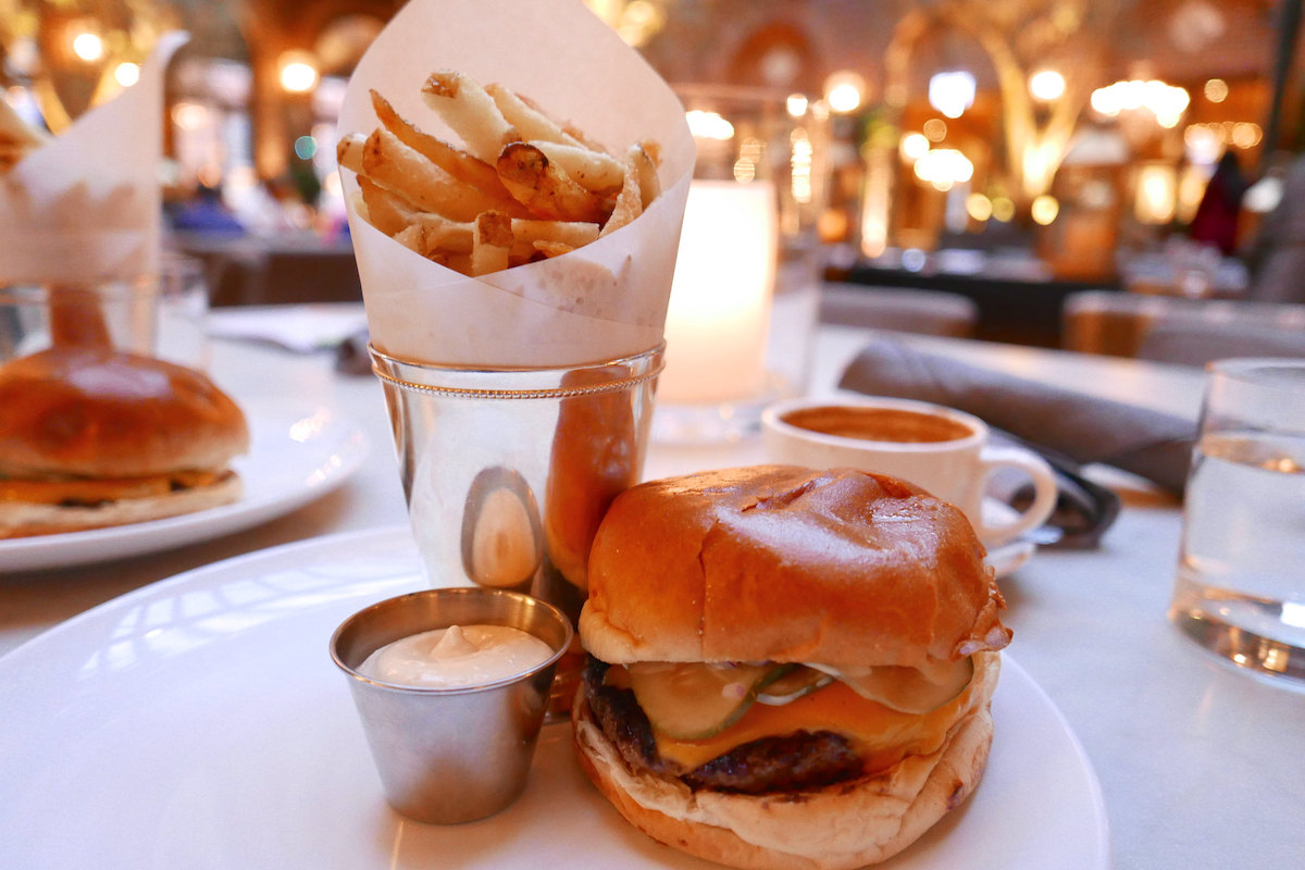 cerca de una hamburguesa gourmet y papas fritas con el hermoso patio del 3 Arts Cafe de Chicago al fondo