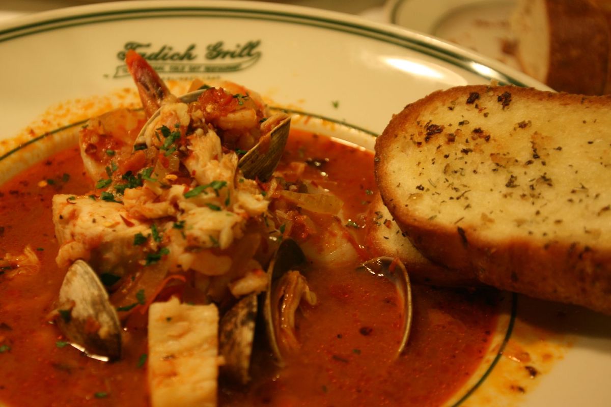 Un excelente primer plano de un tazón de choppino de mariscos con una rebanada de pan en Tadich Grill