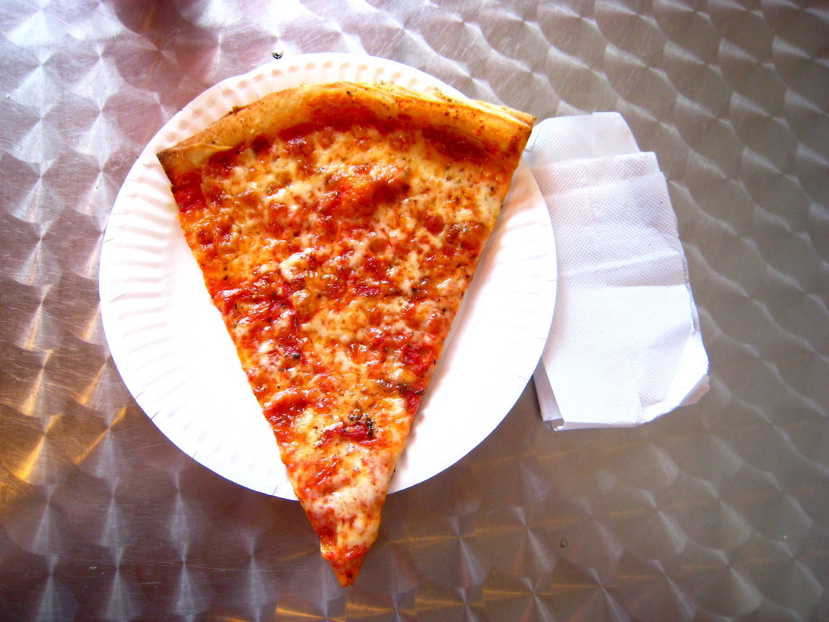 Una rebanada de pizza de queso en un plato de papel blanco es una comida callejera básica en Boston.
