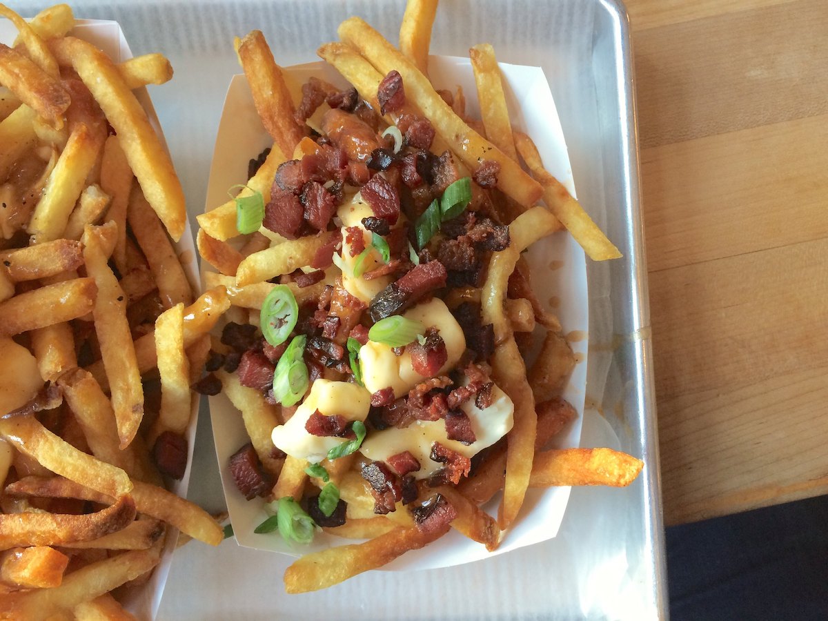 primer plano de dos contenedores de poutine en Saus Boston, un restaurante de comida barata. Las papas fritas están cubiertas con cuajada de queso, trocitos de tocino y cebolla verde