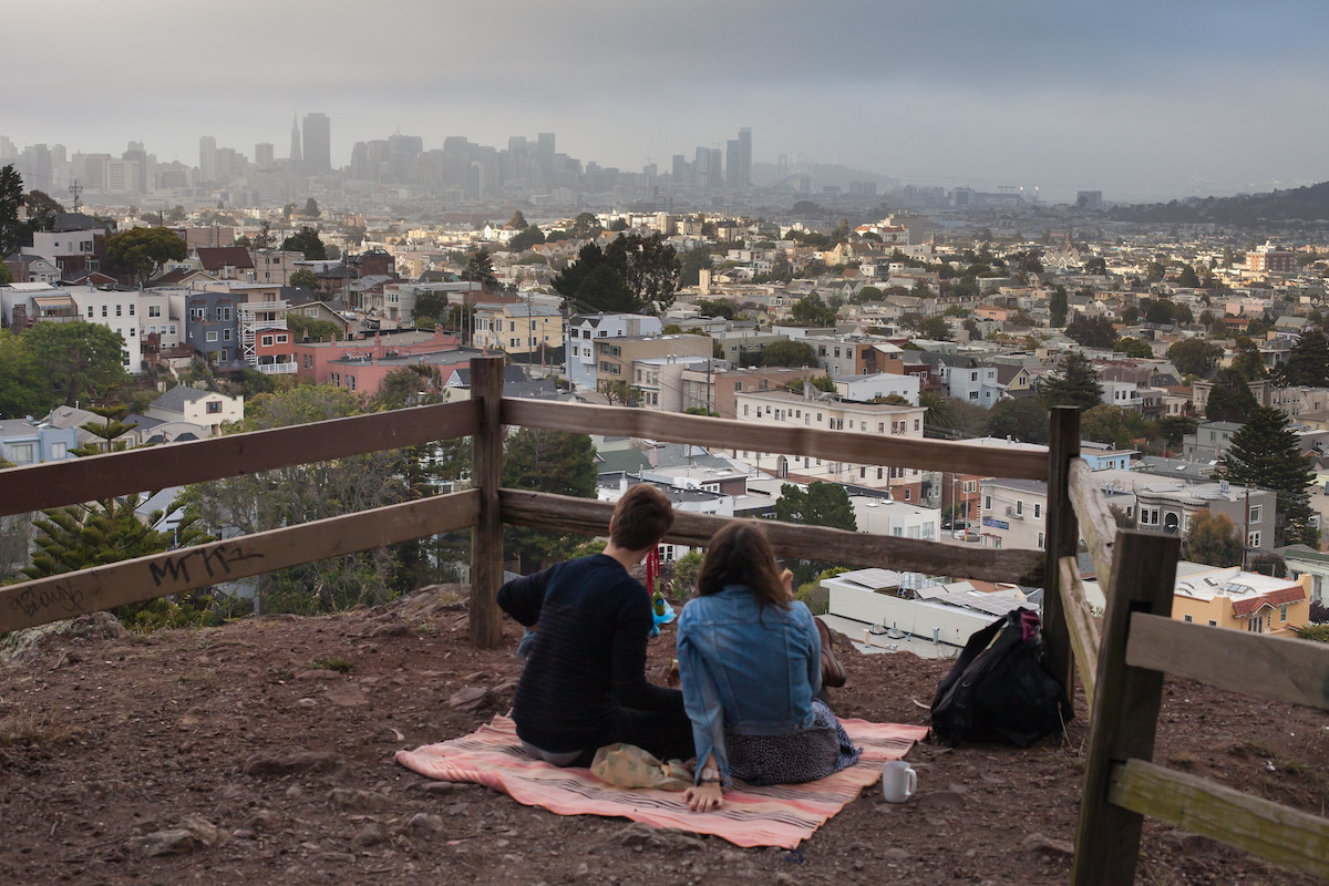 una pareja se sienta en una manta rosa disfrutando de un picnic sobre San Francisco