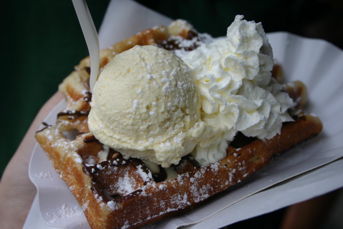 primer plano de una bandeja de papel con un pequeño gofre belga con jarabe de chocolate, una bola de helado y cubierto con crema batida