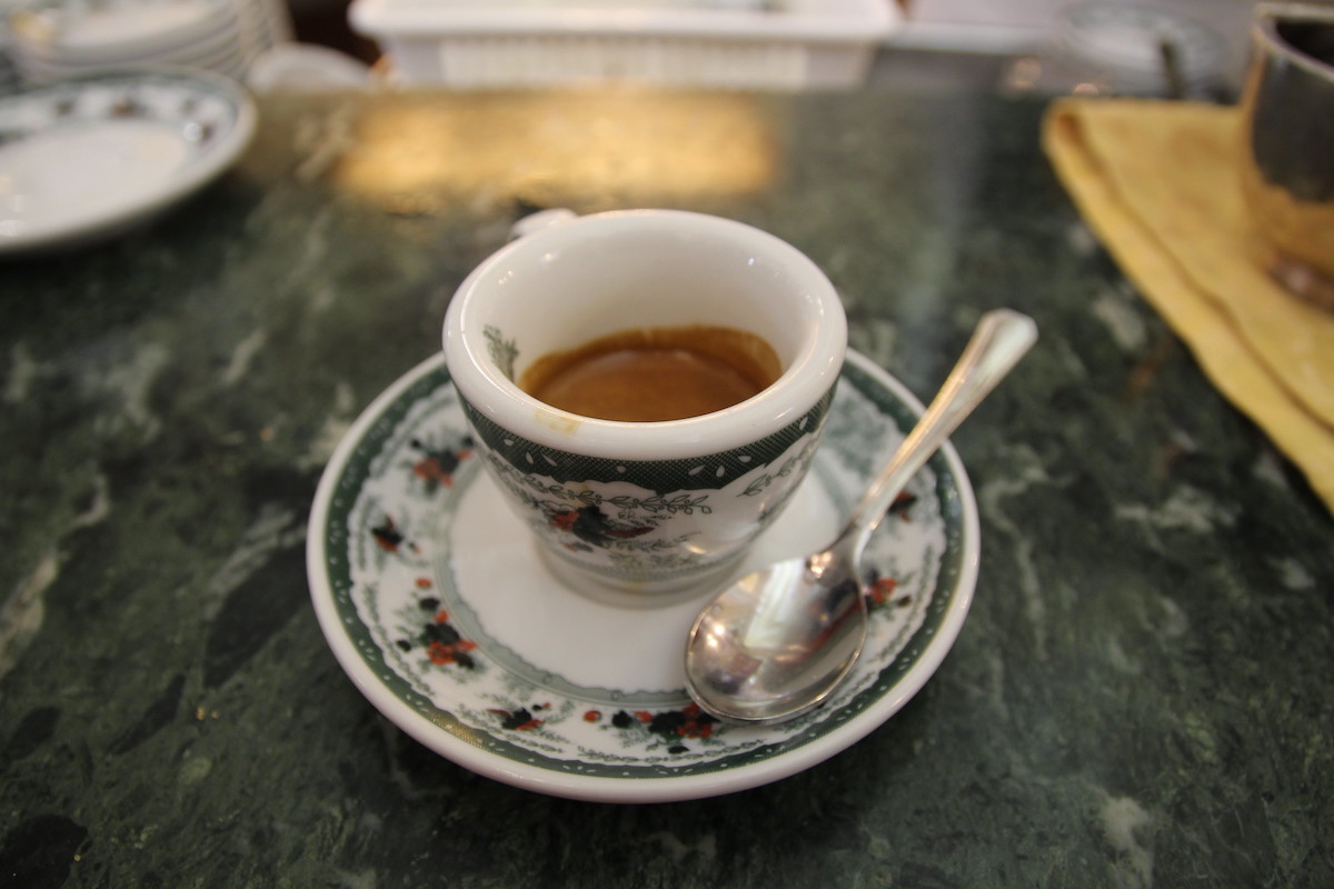 Primer plano de una taza de espresso bellamente decorada y un platillo en un mostrador de café de mármol verde en Gran Caffé Gambrinus en Nápoles, una cafetería clásica