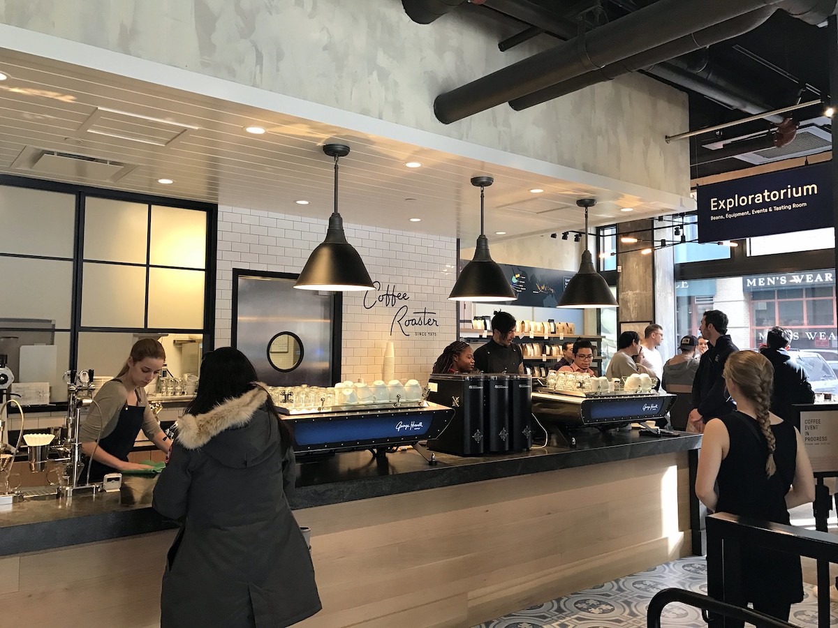 dentro de una cafetería con baristas detrás de la barra y personas tomando pedidos