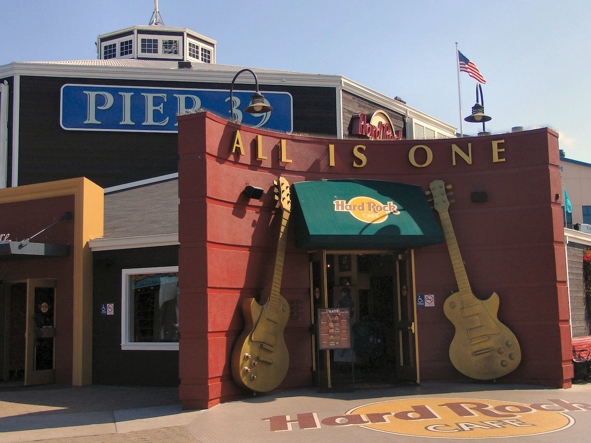 Foto de la entrada al restaurante Hard Rock Cafe en el muelle 39 de San Francisco. Dos guitarras doradas enmarcan la puerta de un edificio rojo con un toldo verde