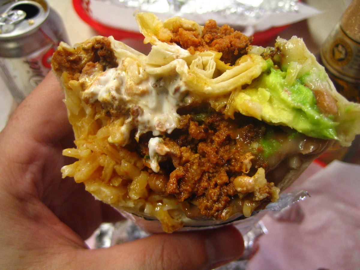 Primer plano de una sección transversal de un burrito estilo Misión, una comida por la que se conoce a San Francisco. El burrito se rellena con arroz, chorizo, crema agria y guacamole.