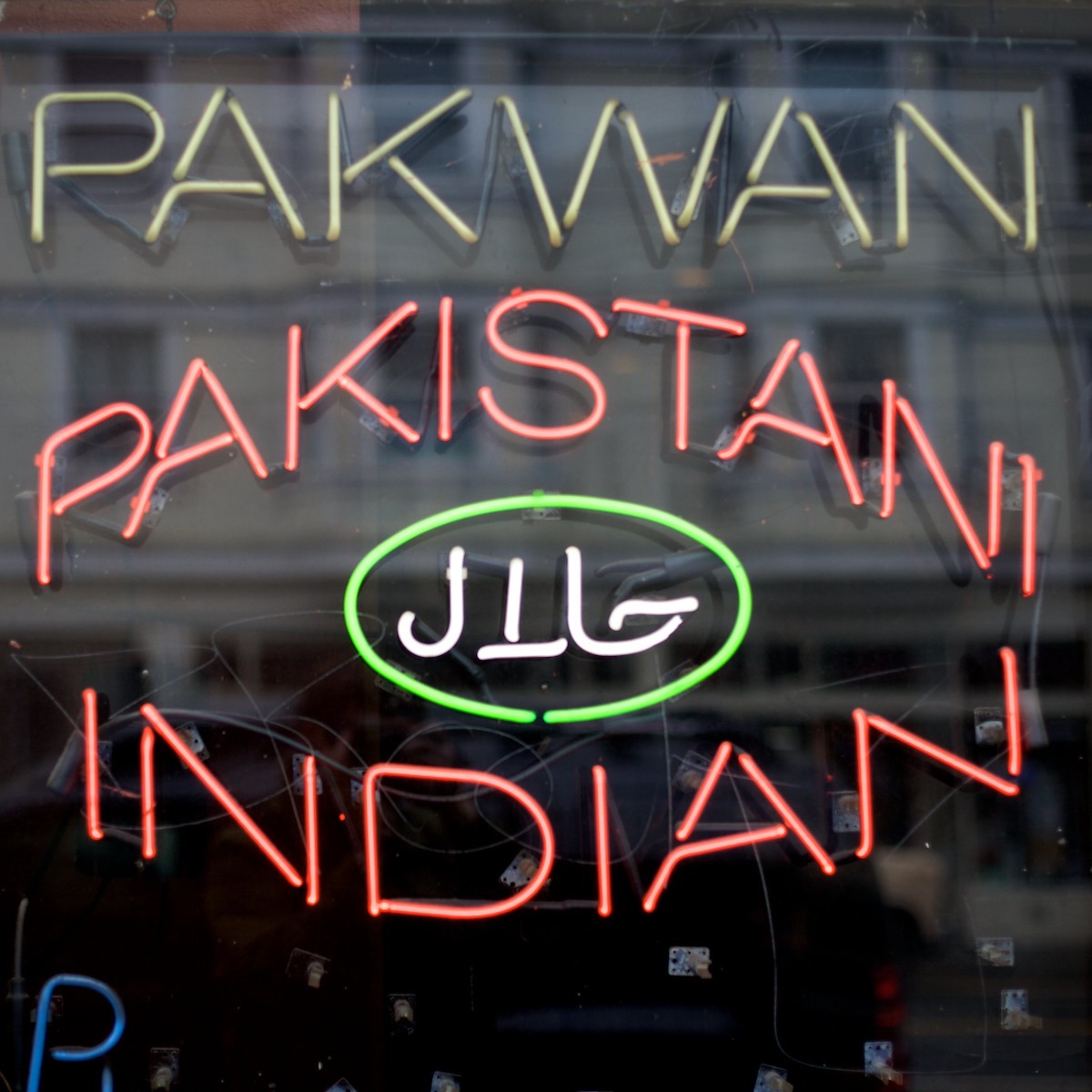 cierra un letrero de neón en la ventana de un restaurante. Las letras amarillas dicen "Pakwan" y las letras debajo dicen "Indio de Pakistán"