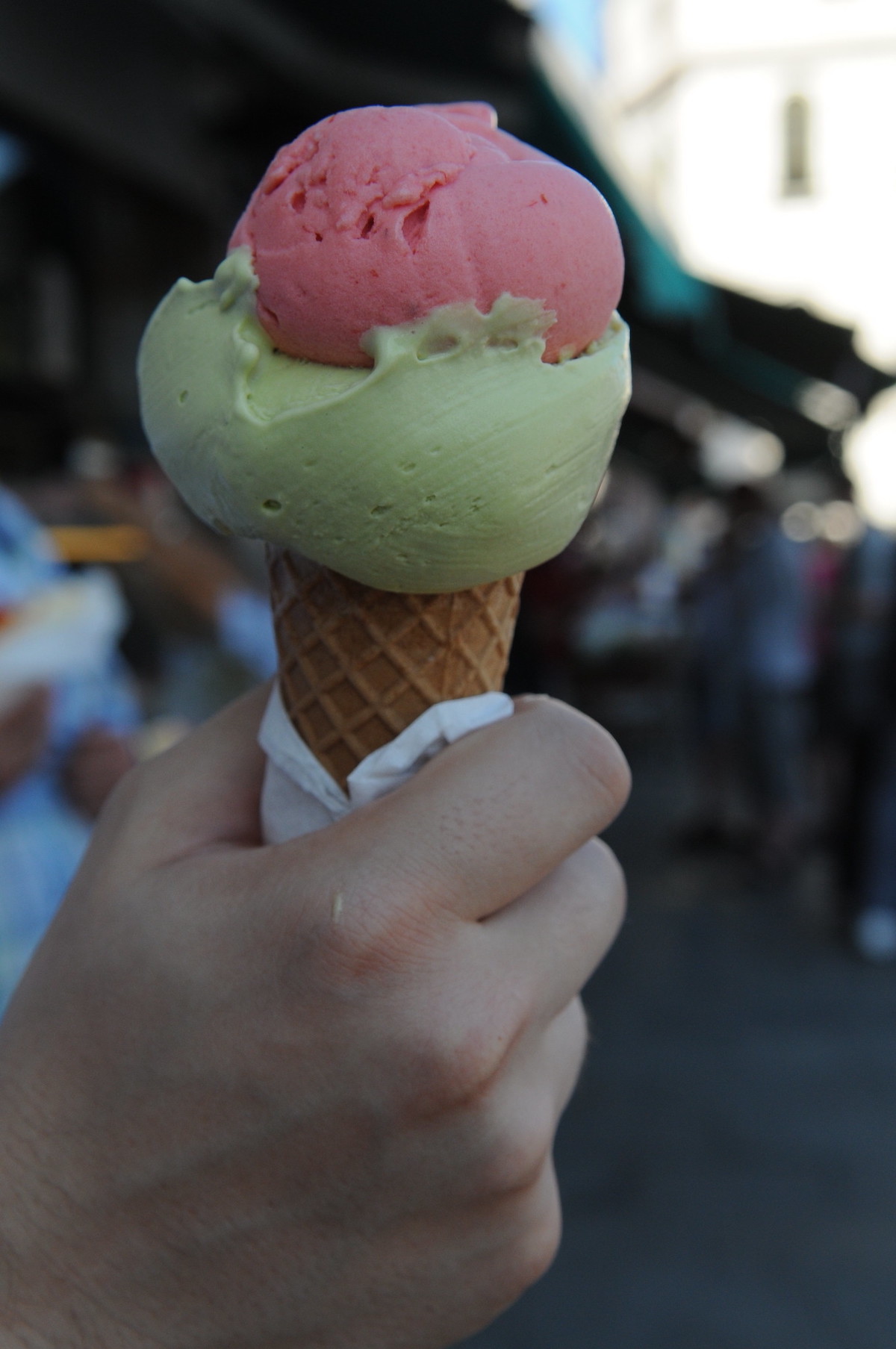 primer plano de una persona sosteniendo un cono con dos bolas de helado, uno verde claro y otro rosa
