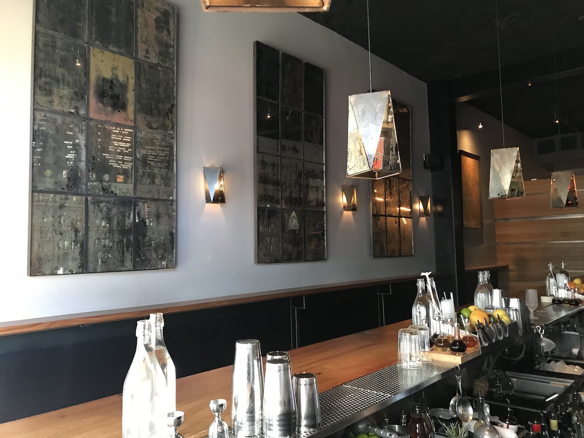 Toma interior desde la parte trasera del bar ABV, un bar de cócteles en San Francisco. Paneles de espejos restaurados adornan las paredes, reflejando los estantes del bar y el menú en la pared