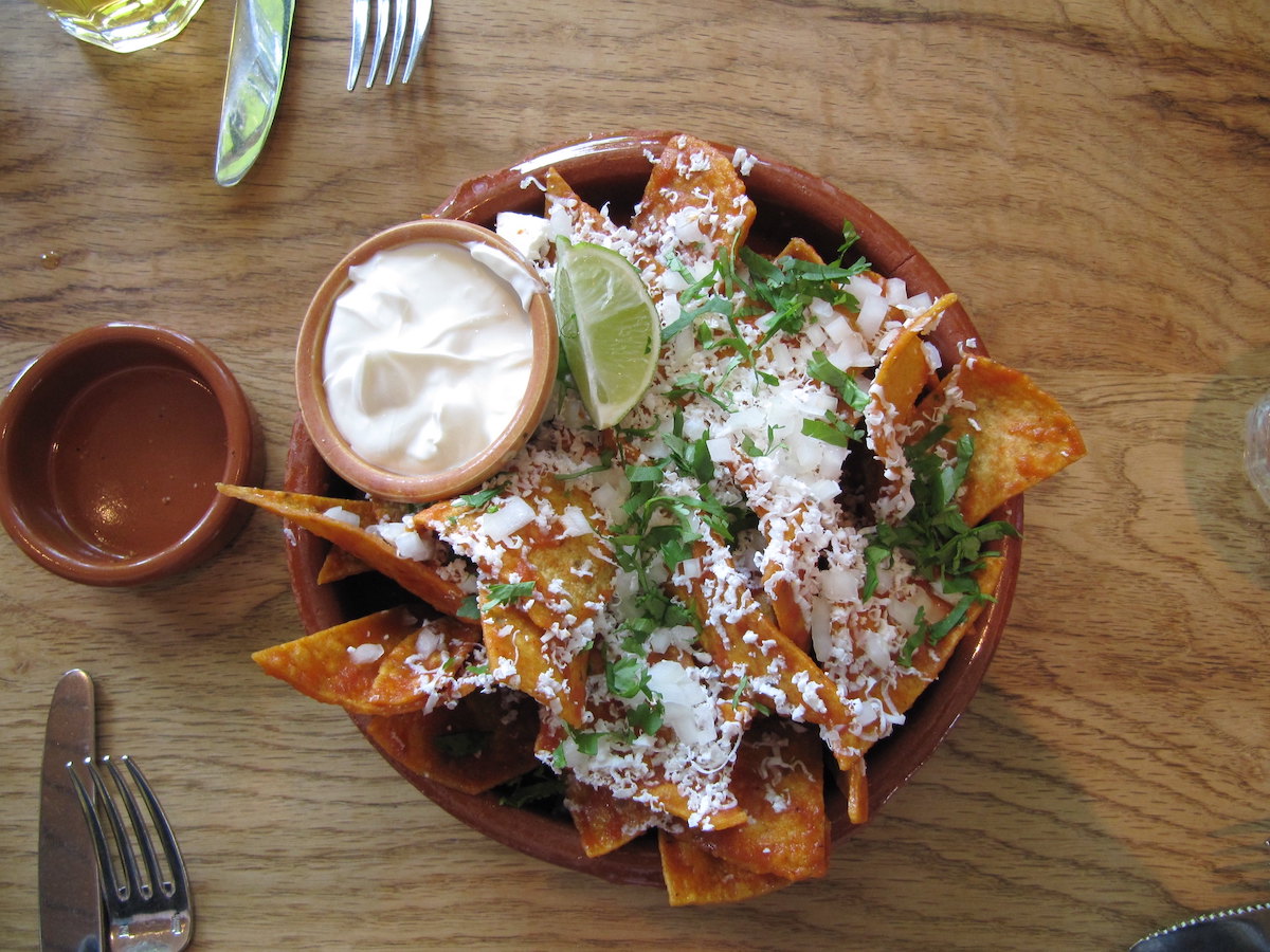 tazón de papas fritas adornado con queso, rodaja de lima, cilantro y salsas