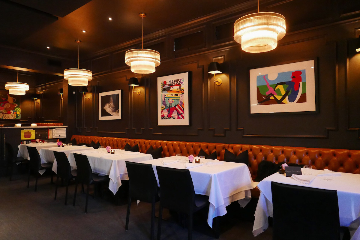 Foto interior del comedor de California, uno de los mejores restaurantes de San Francisco. Las mesas con manteles blancos se alinean a lo largo de una larga cabina de cuero marrón. Las paredes están pintadas de negro y coloridas obras de arte abstractas cuelgan de las paredes.