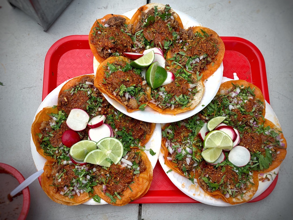 Tres platos con 5 tacos pequeños, rábanos y lima en una bandeja roja