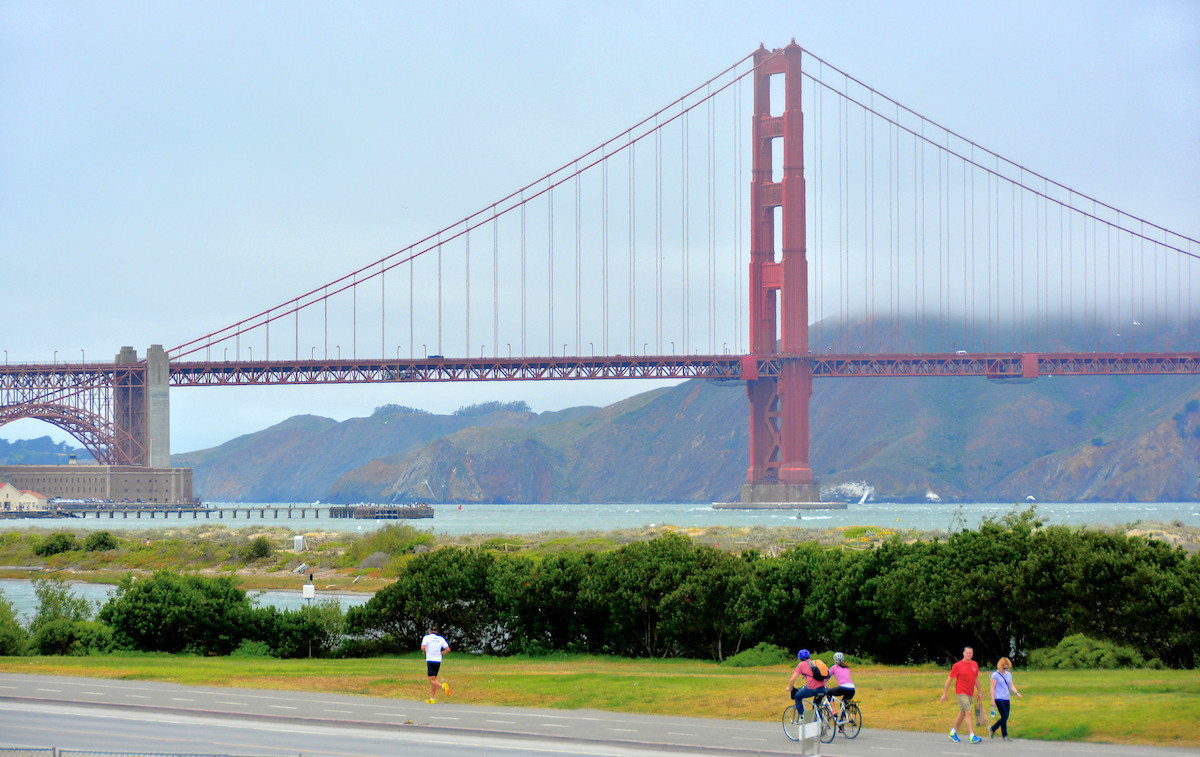 La gente trota, camina y anda en bicicleta por un sendero en Crissy Field en San Francisco con el puente Golden Gate al fondo.