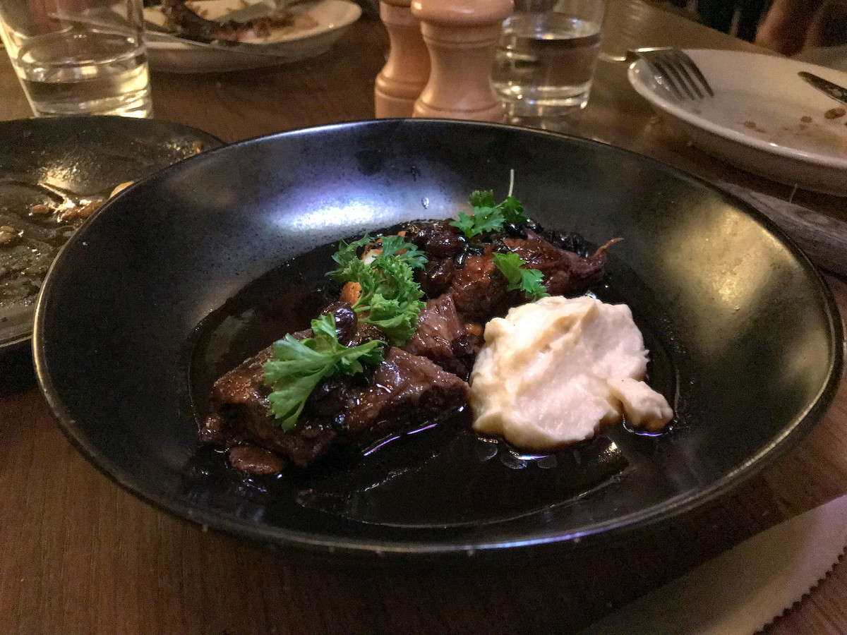 costilla de ternera con puré de patatas en un plato negro