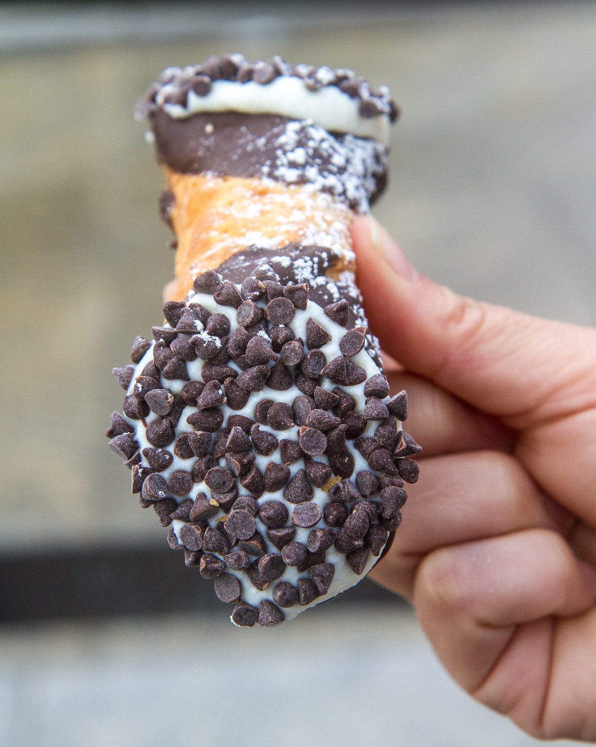 primer plano de una persona con un cannoli cubierto con trocitos de chocolate
