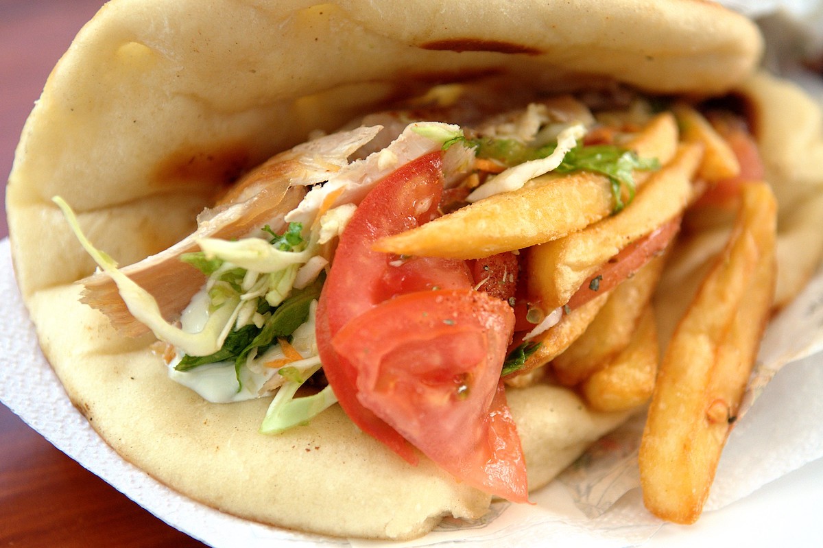Un primer plano de un gyro griego, pan de pita plano doblado para encerrar trozos de pollo, tomates, verduras y papas fritas cubiertas con una salsa cremosa