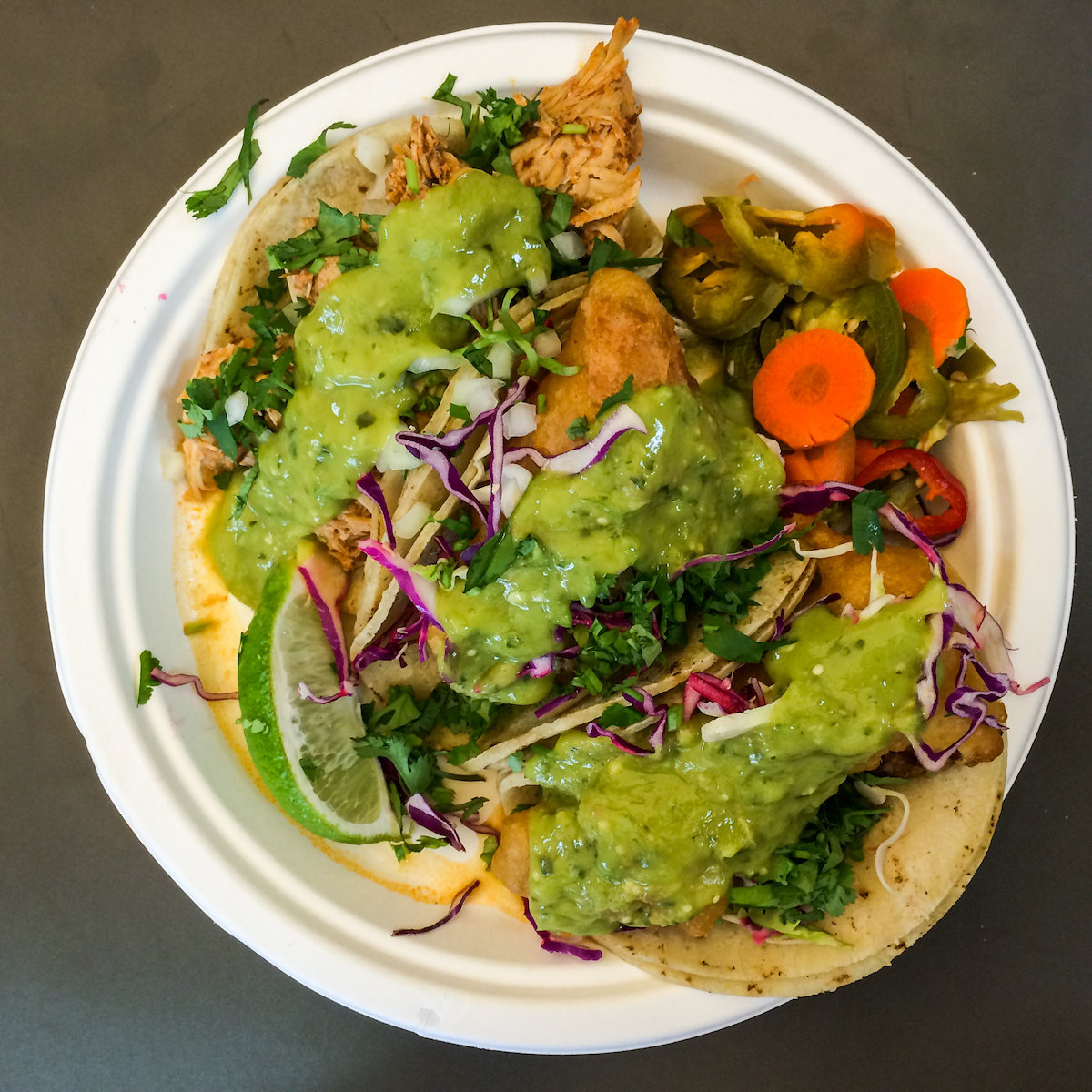 plato de papel cargado con tres tacos cubiertos de guacamole