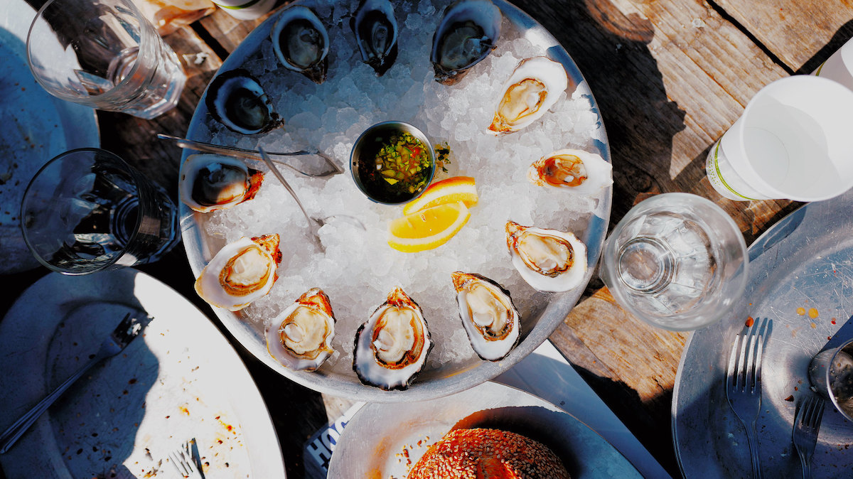 Fotografía cenital de una mesa de comedor en Hog Island Oyster Co. en San Francisco. Hay ostras crudas en media concha en una bandeja redonda llena de hielo. Las ostras del Pacífico son un alimento por el que San Francisco es famoso.