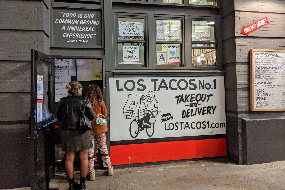 La gente busca comida fuera de un puesto de tacos de color gris