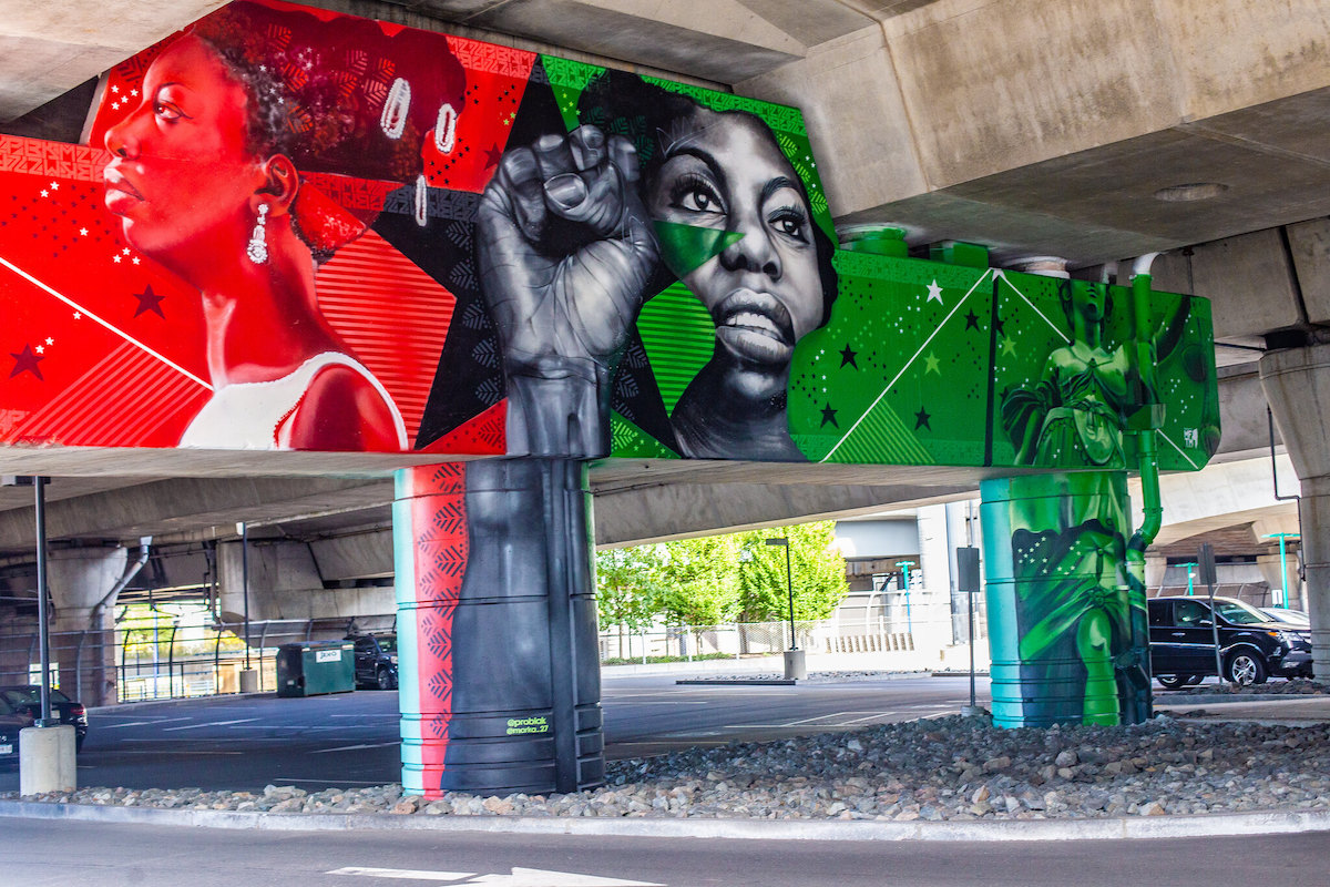 Arte callejero detallado pintado bajo un paso elevado. Fondos rojos y verdes brillantes con figuras de mujeres negras poderosas