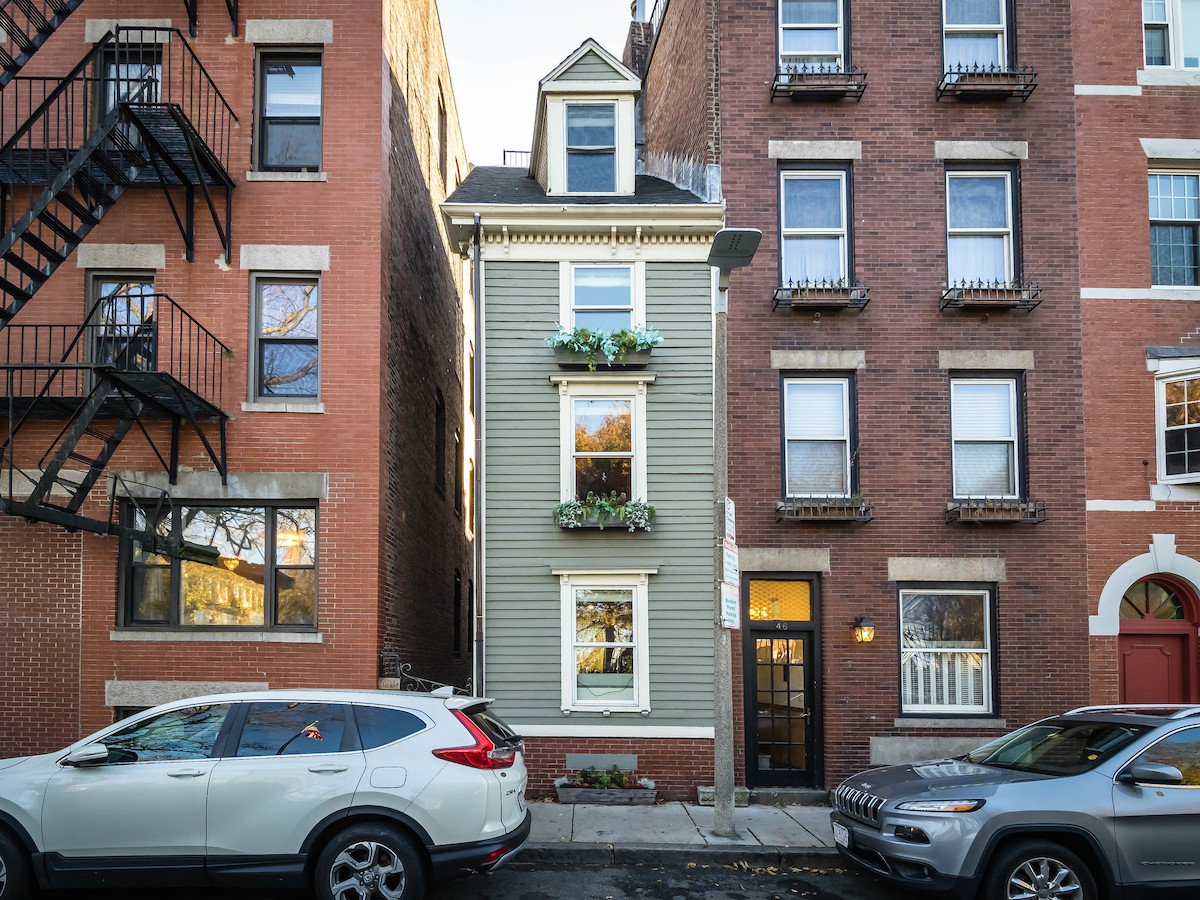 Una casa estrecha de tres niveles pintada de verde con flores saliendo de las jardineras. La casa está entre dos edificios de ladrillo ordinarios. Una casa tan delgada que es una verdadera joya escondida de Boston