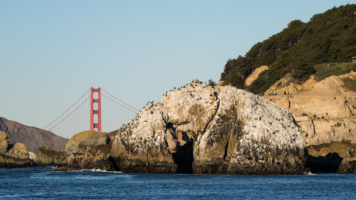 Grandes rocas en el agua y acantilados cubiertos de árboles en el Parque Nacional Lands End con el puente Golden Gate al fondo