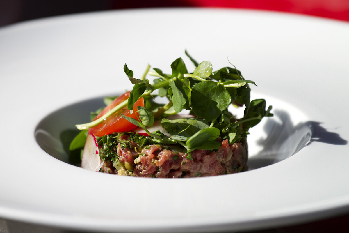un primer plano de un plato blanco con bistec tártaro y verduras encima
