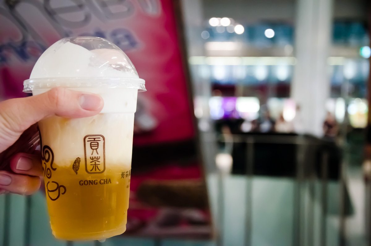 primer plano de una persona que sostiene un vaso de plástico lleno de té helado dorado con el restaurante borroso en el fondo