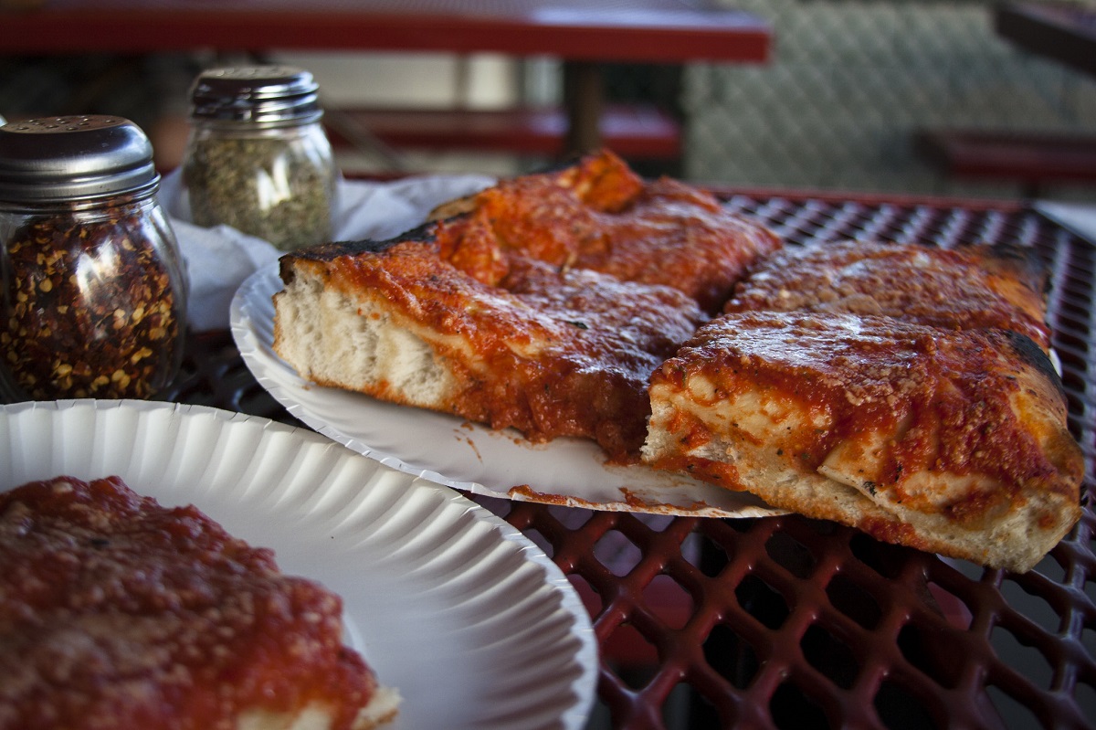 Los cuadrados de pizza se sientan en platos de papel que descansan sobre una mesa de picnic al aire libre