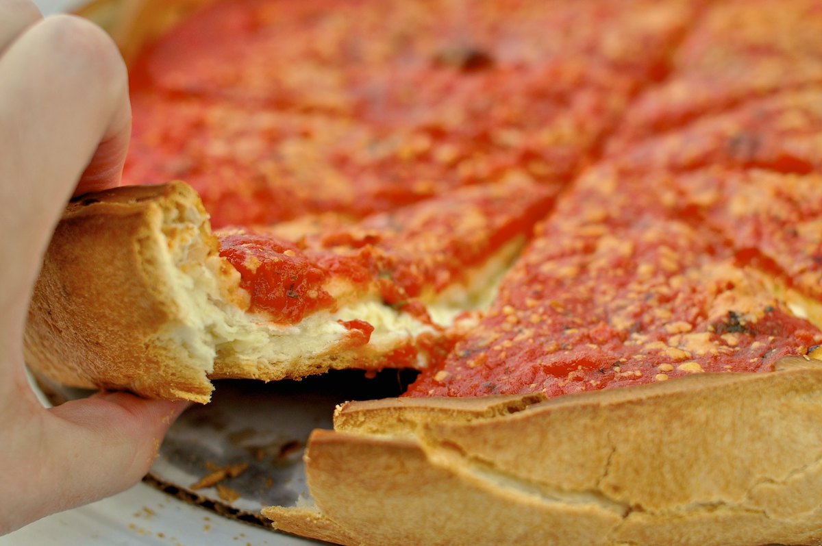 cerca de una pizza de plato hondo de Chicago, con una mano acercándose para tomar una porción