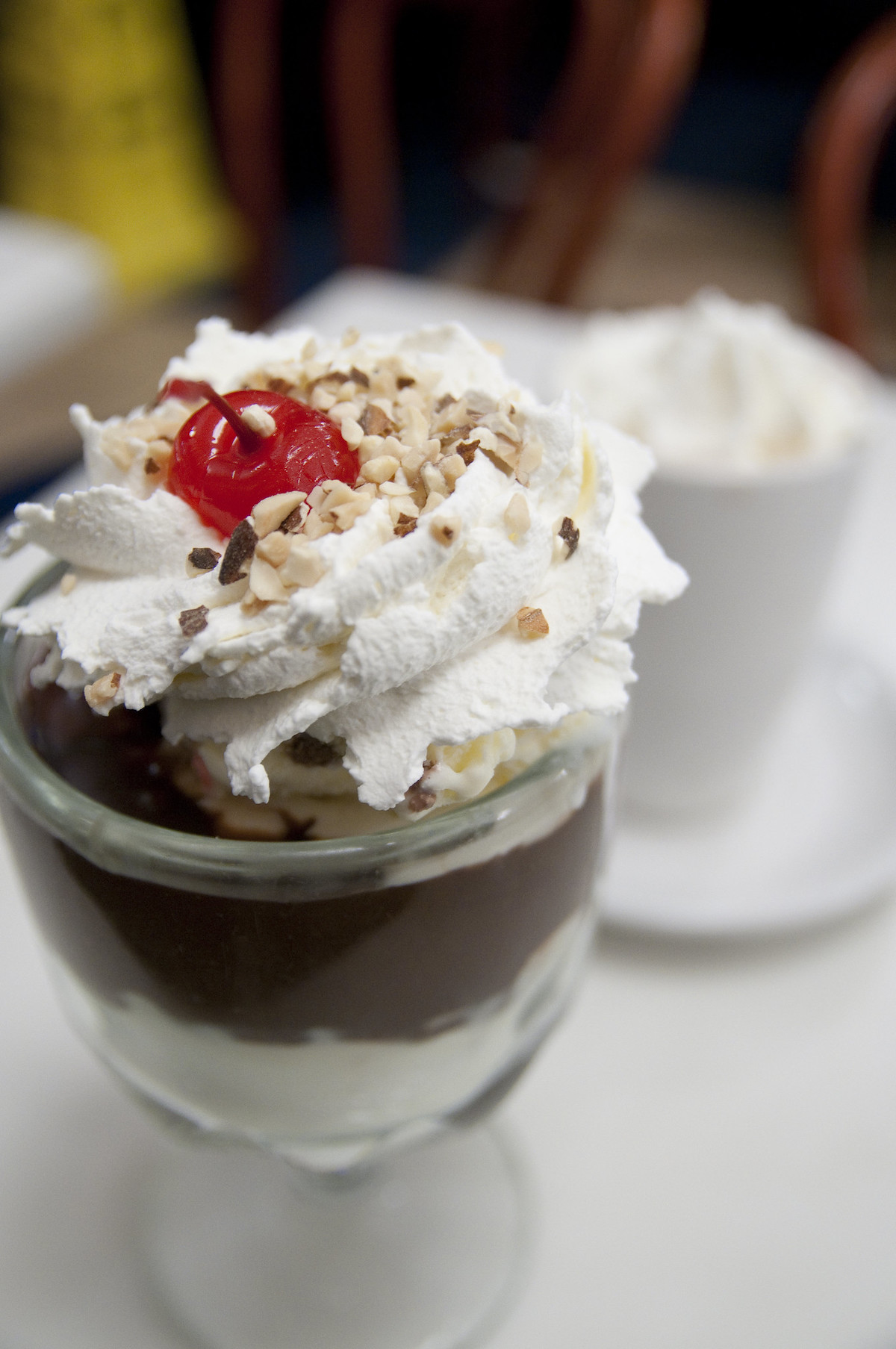 Primer plano de un helado con chocolate caliente en un recipiente de vidrio transparente, con crema batida y cerezas.