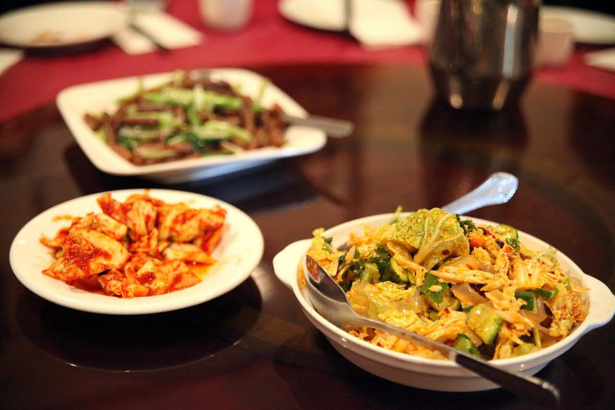 Tres platos de comida china en Fu Run en Nueva York se sientan en una mesa de madera oscura