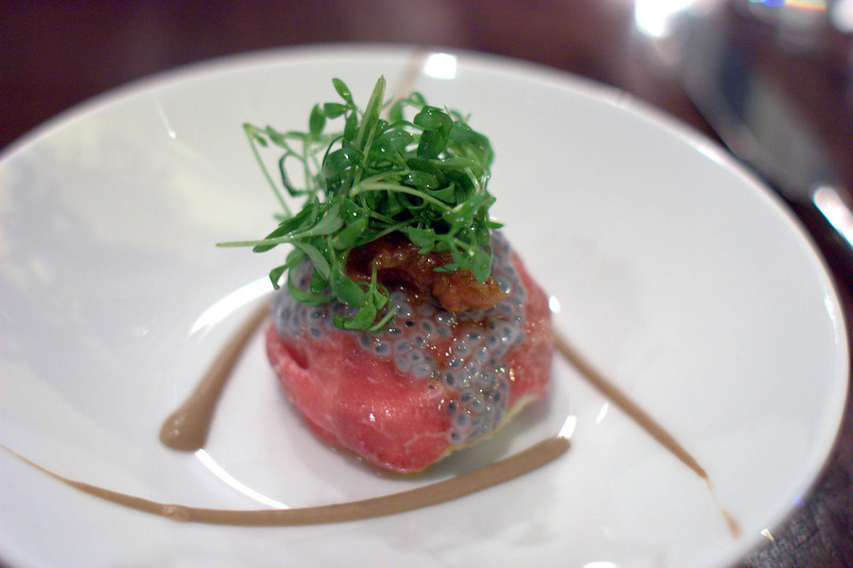 Un gran cierre de un lugar blanco con un pequeño trozo de carpaccio de ternera cruda, con verduras en él
