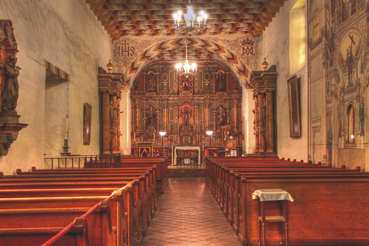 Disparo dentro de la iglesia en Mission Dolores. Los asientos de madera se alinean frente al púlpito profusamente decorado.