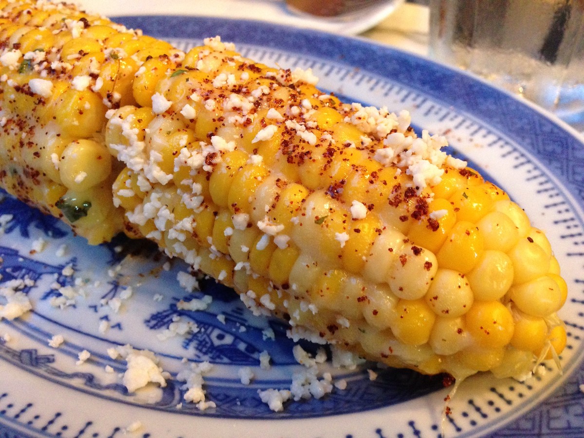 muy cerca del maíz callejero mexicano en un plato azul y blanco. El maíz se espolvorea con condimento rojo y queso falso blanco.