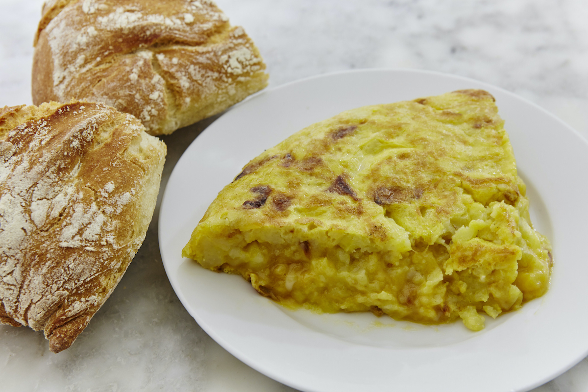 Un trozo de tortilla de patata en un plato blanco junto a dos panecillos