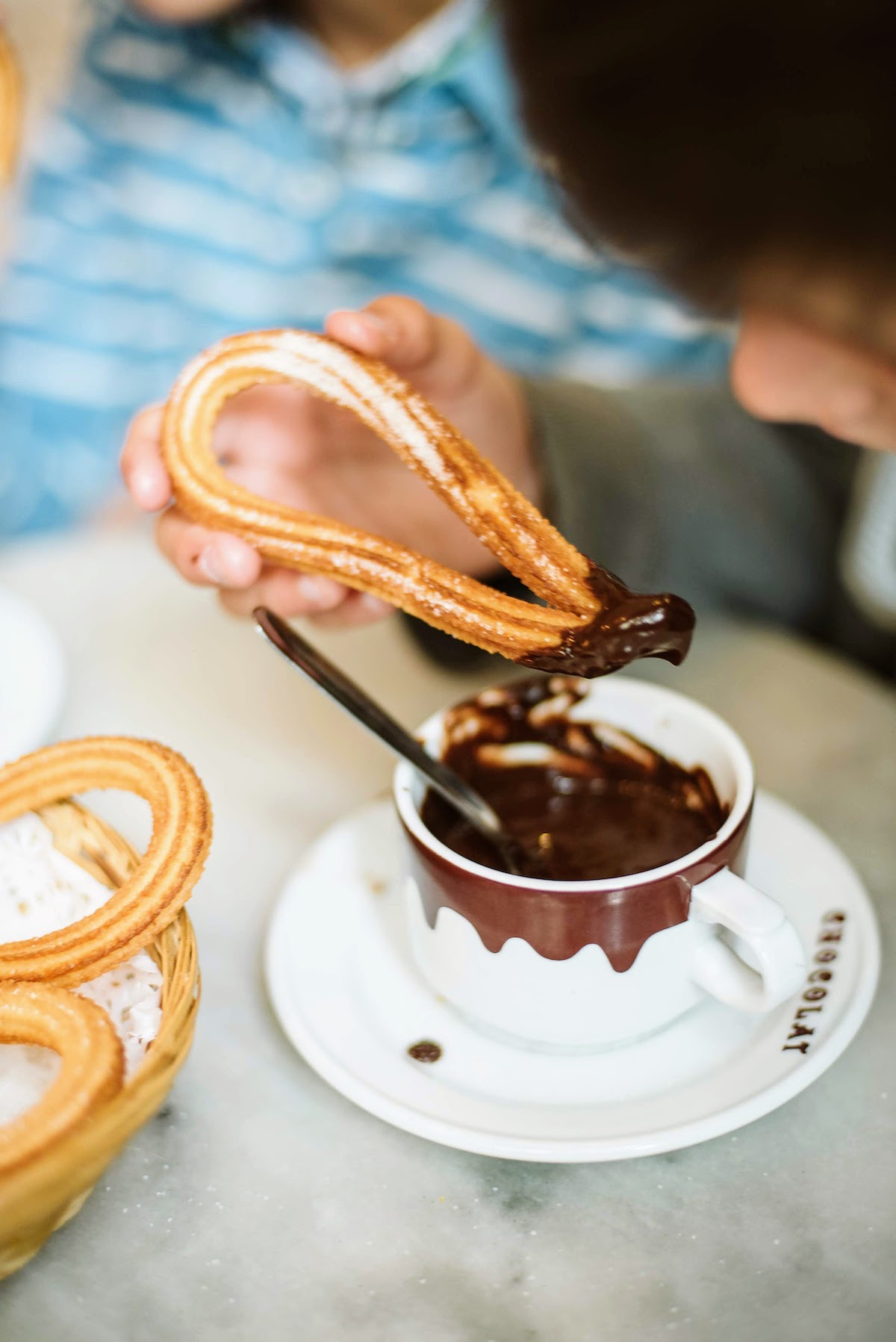La mano de un niño mojando churros cubiertos de azúcar en una taza gruesa de chocolate caliente