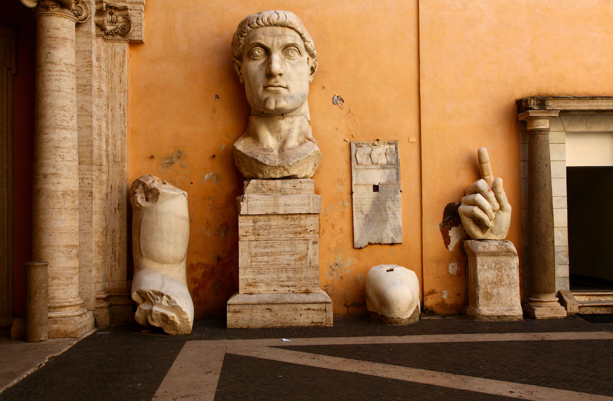 Columnas de mármol de la antigua Roma, la cabeza de una estatua del emperador Constantino y otros fragmentos expuestos contra una pared naranja.