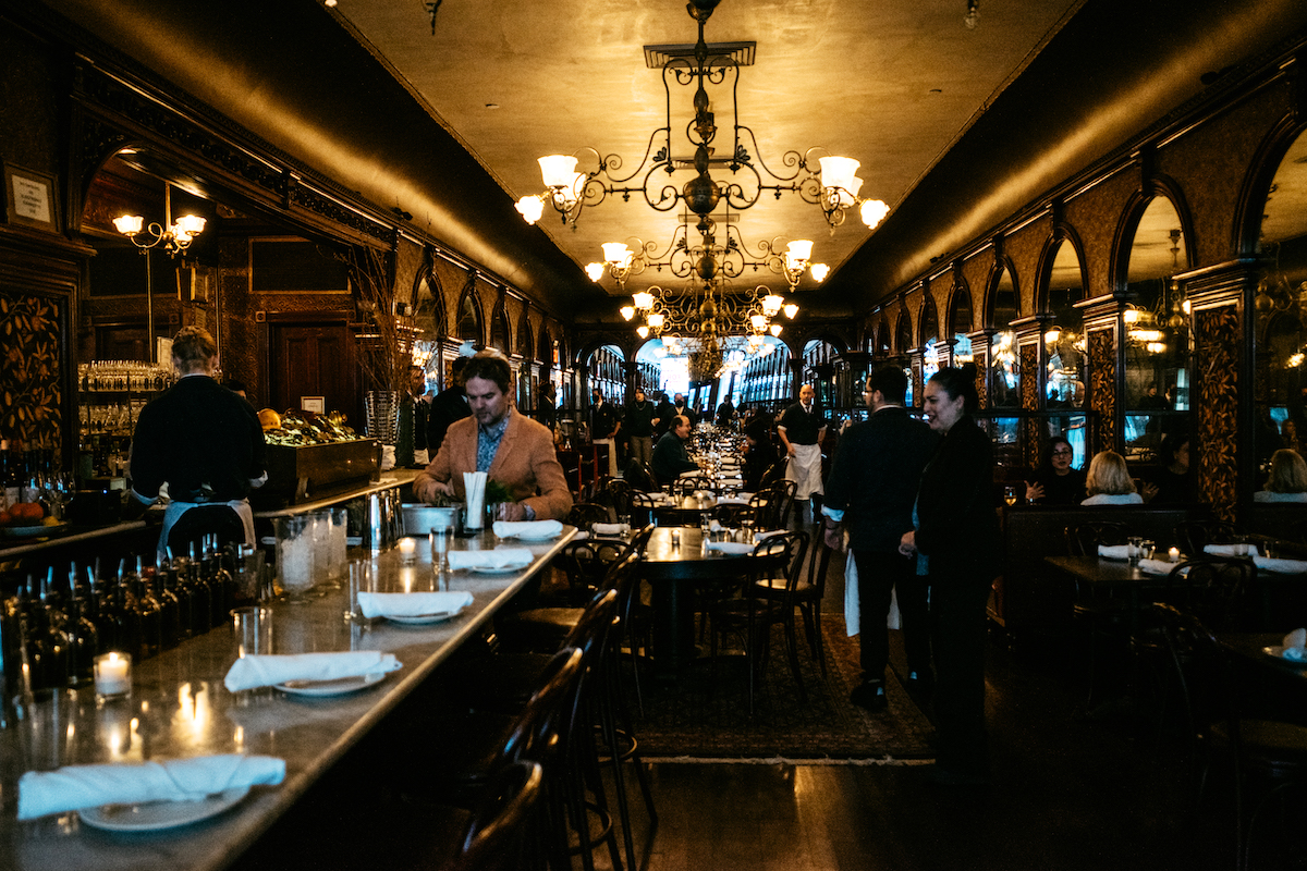 Interior de un asador de Nueva York con lámparas antiguas y asientos junto a una barra de mármol.