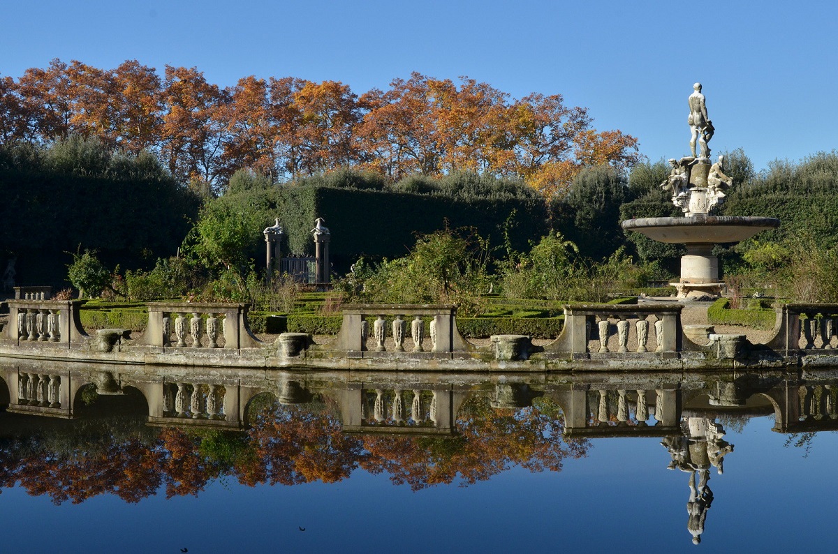 Una gran piscina rodeada de estatuas de piedra y columnas con árboles de colores otoñales