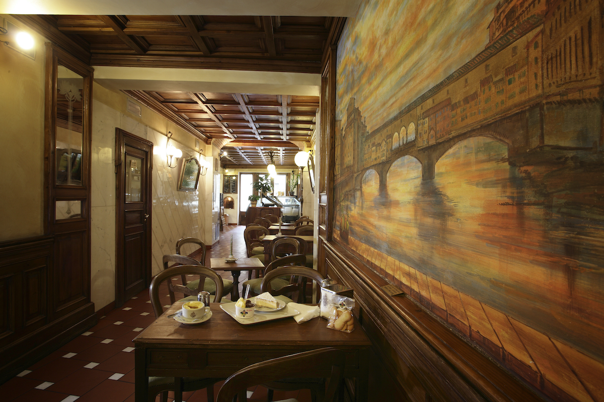 Interior de una heladería histórica con paneles de madera oscura y una pintura de un puente en la pared de la derecha