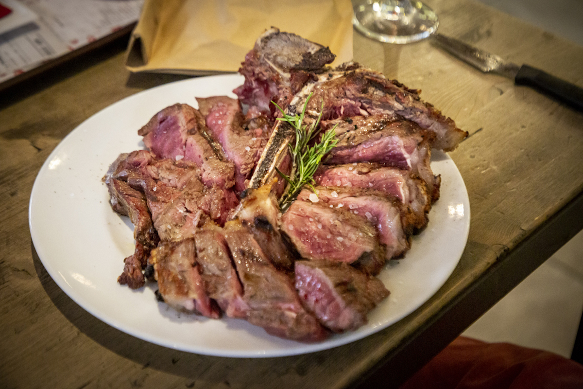 Cierra el bistec florentino aderezado con hierbas y espolvoreado con sal marina en un plato blanco